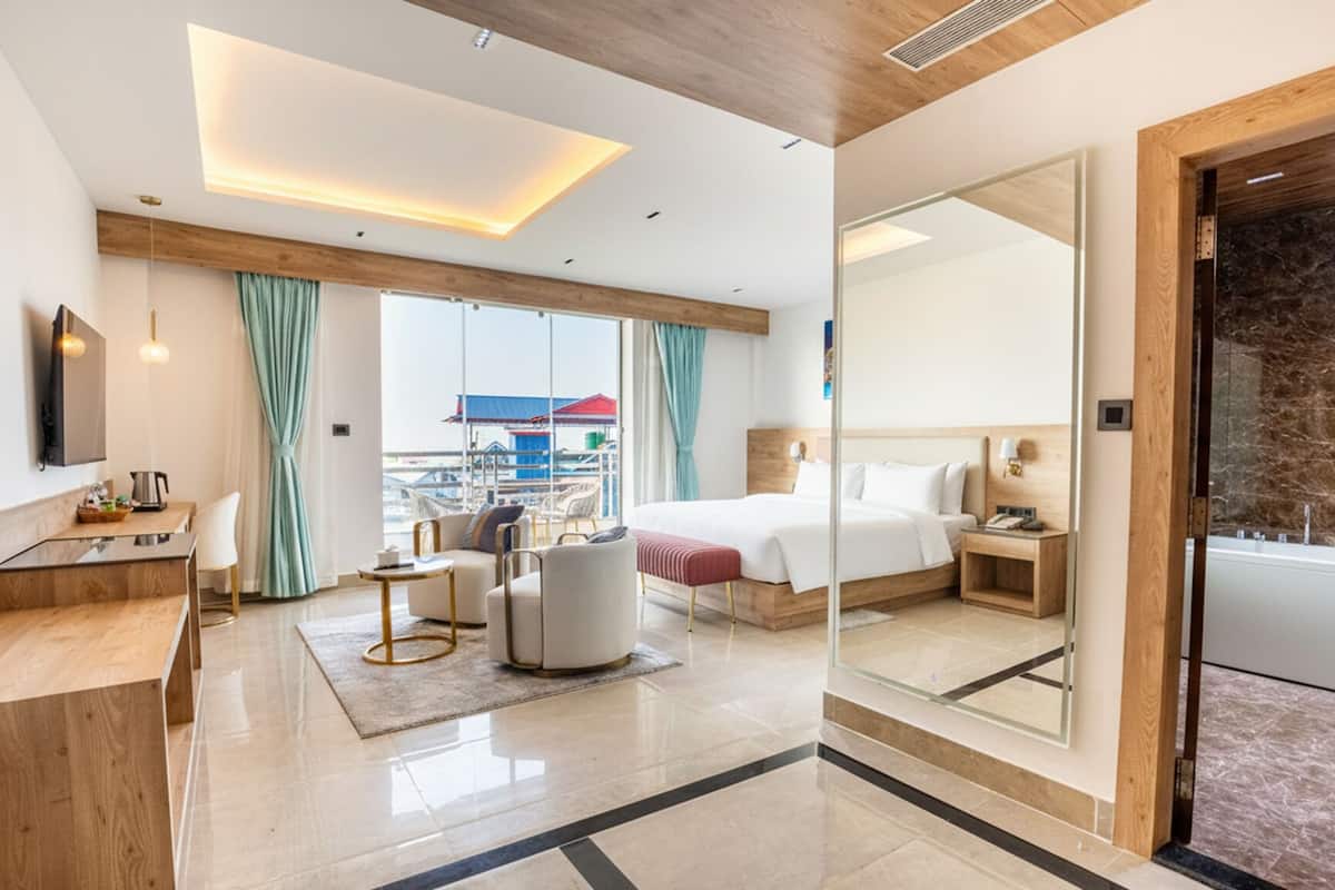A modern hotel room with a bed, a desk, a chair, a sofa, a small table, and a large mirror.