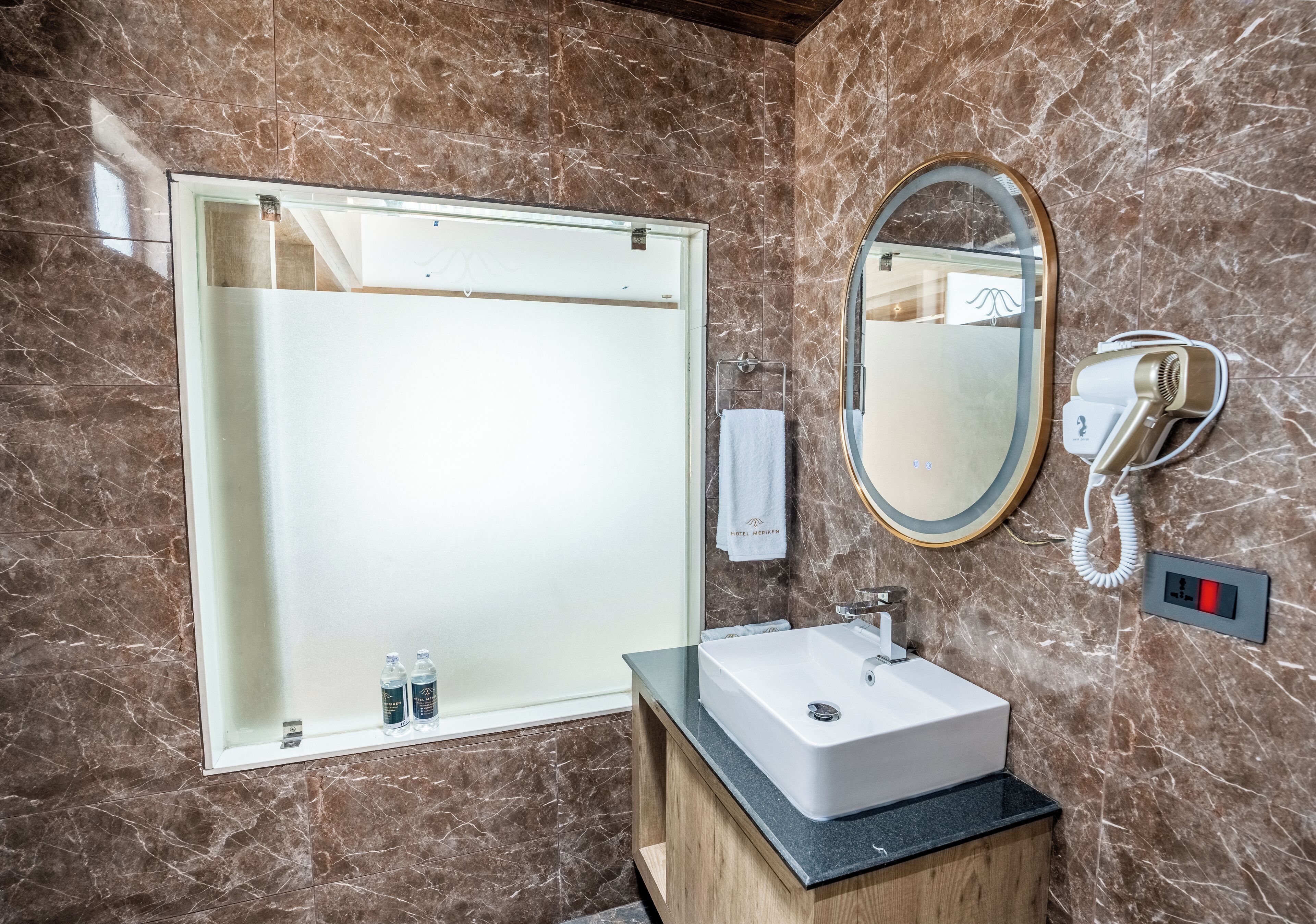 A bathroom with a marble wall, a large mirror, a sink, and a towel rack.