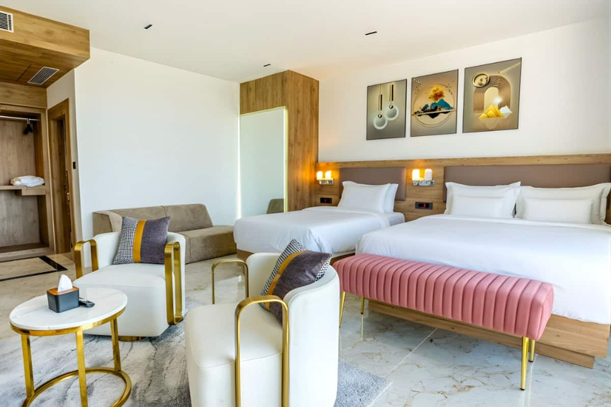 A hotel room with two beds, a sofa, a round table, and a small desk.