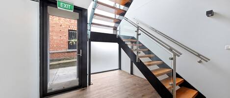 A modern interior with a wooden staircase, a glass door leading outside, and a visible exit sign.