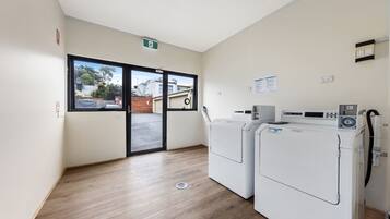 A laundry room with two front-loading washing machines, a dryer, and a window with a view of the outside.