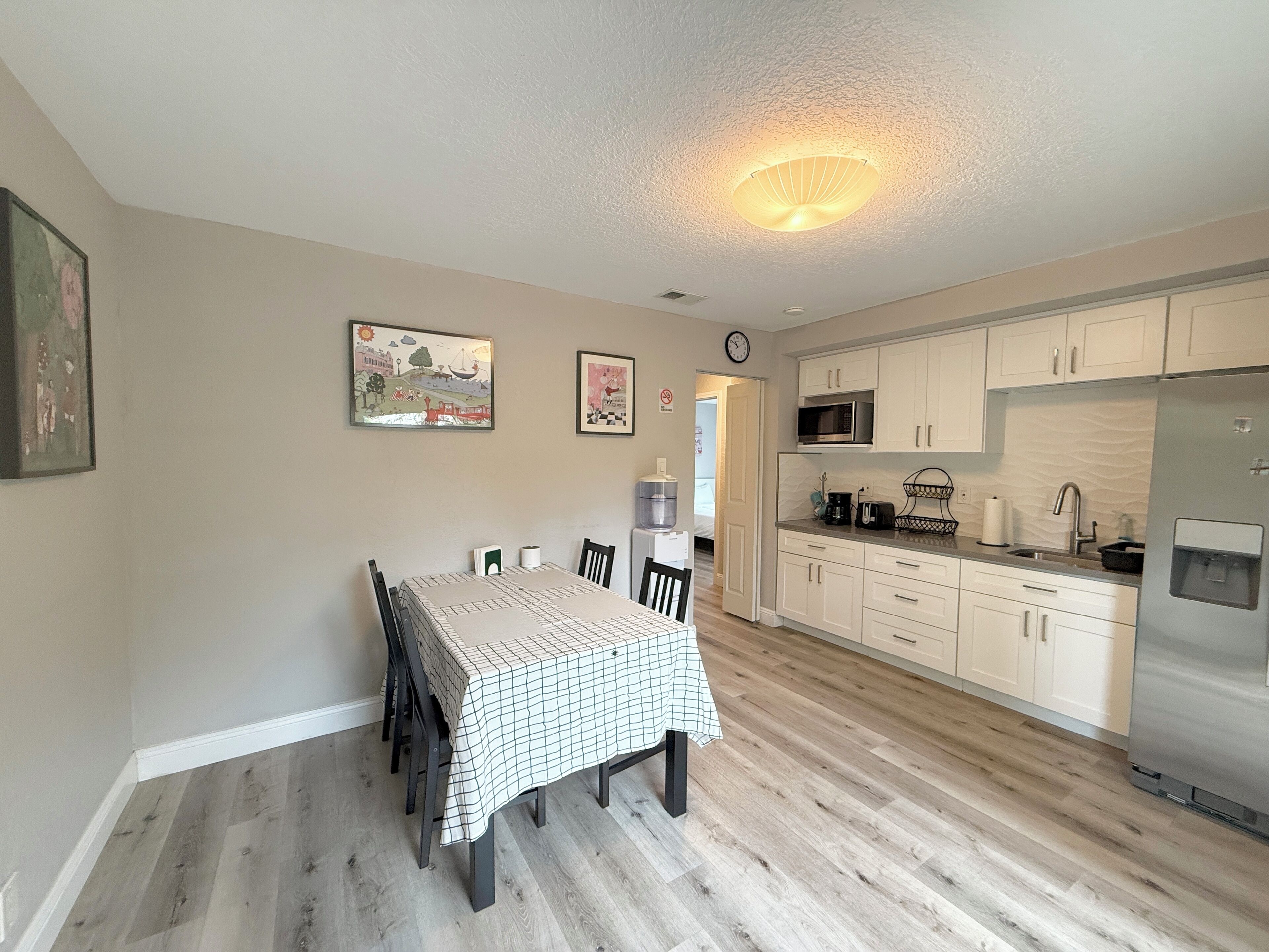 A modern kitchen with white cabinets, a stainless steel refrigerator, and a dining area with a table and chairs.