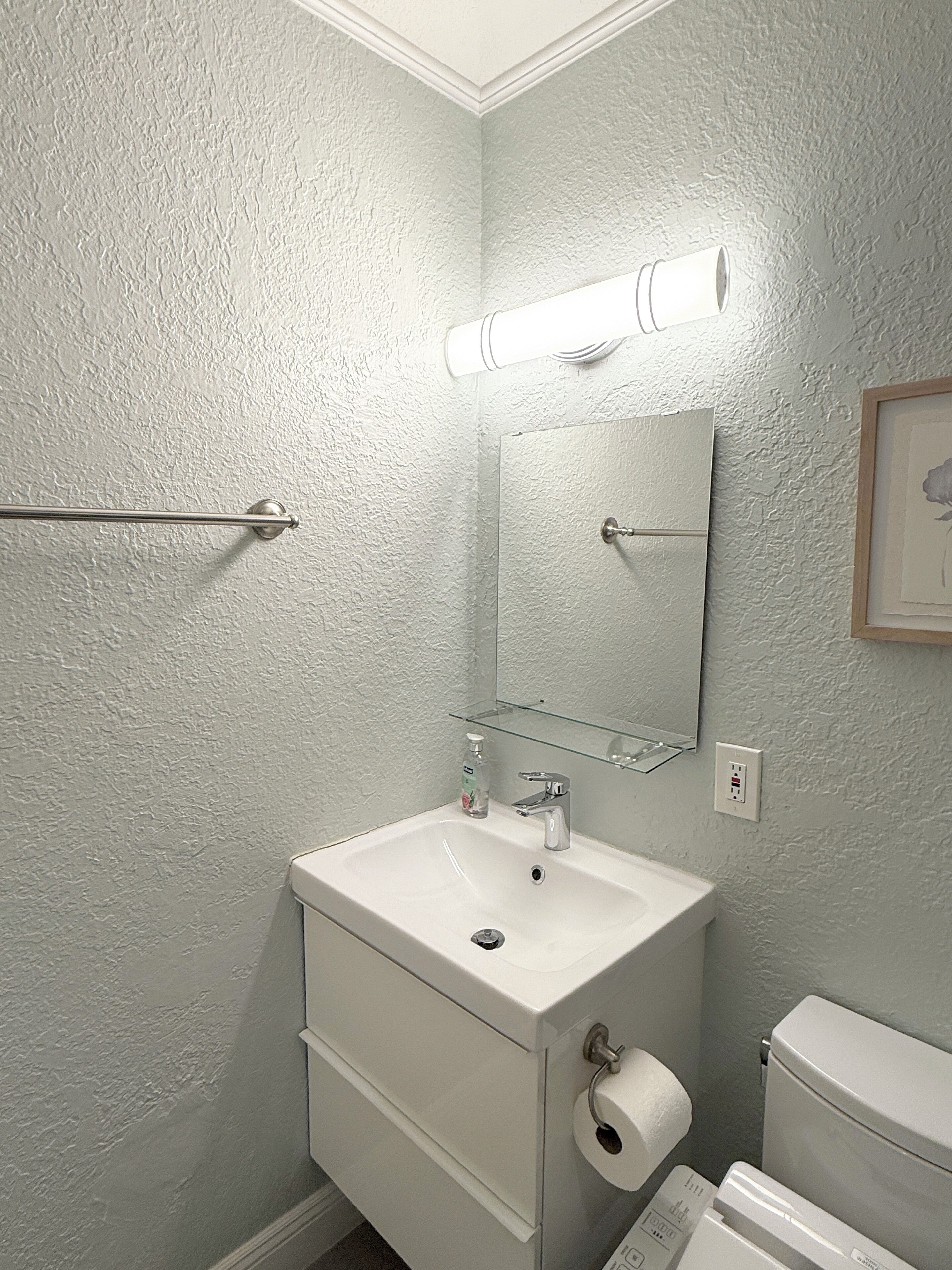 Une salle de bain avec un lavabo, un miroir et des toilettes, le tout de couleur blanche.