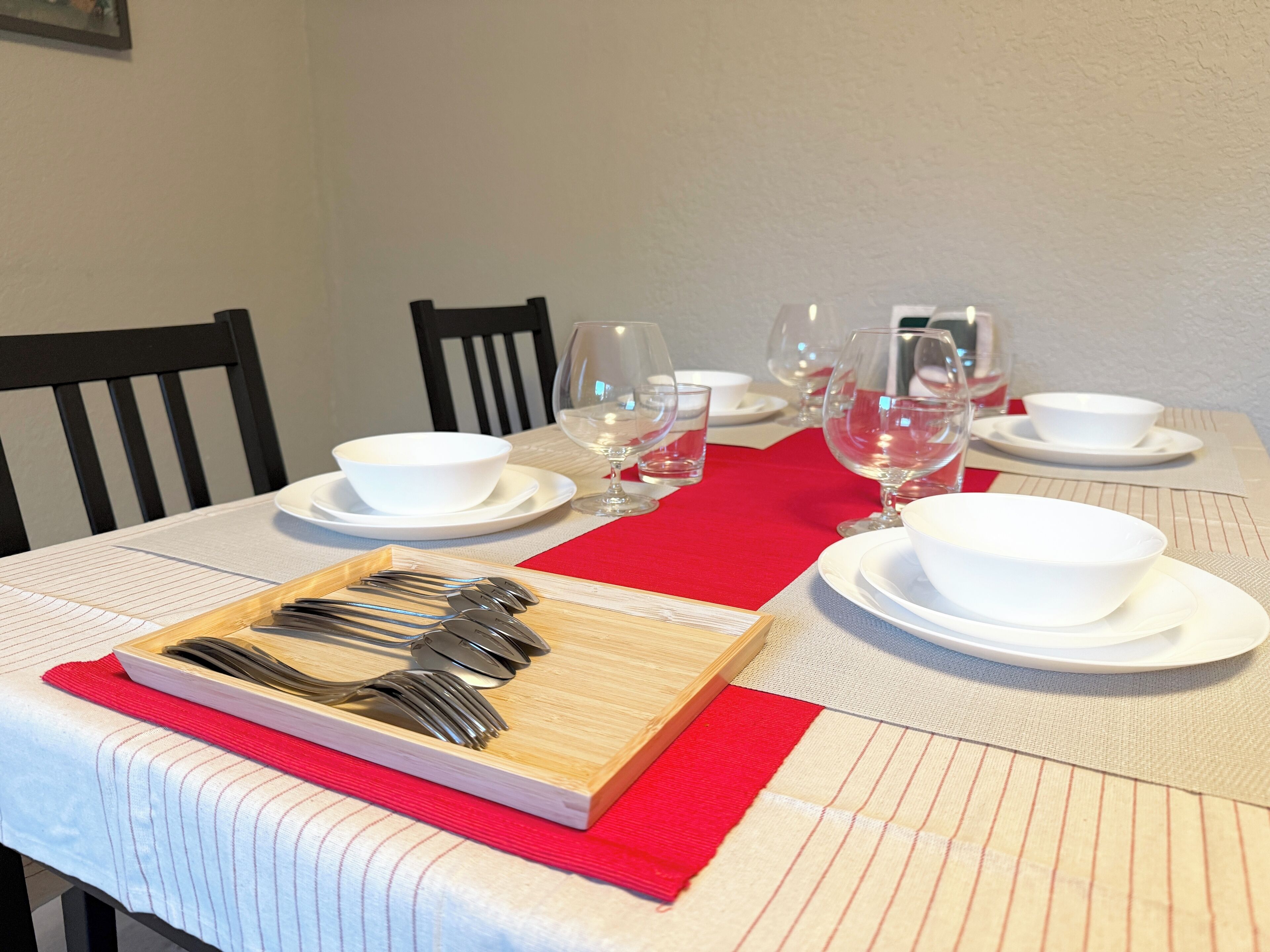 Une table à manger dressée avec des assiettes blanches, des verres à vin et des couverts, le tout posé sur une nappe à rayures.