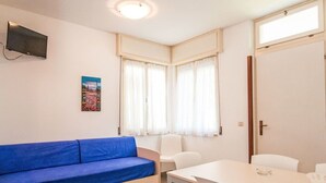 Une pièce avec un canapé bleu, une table blanche et un téléviseur fixé au mur.