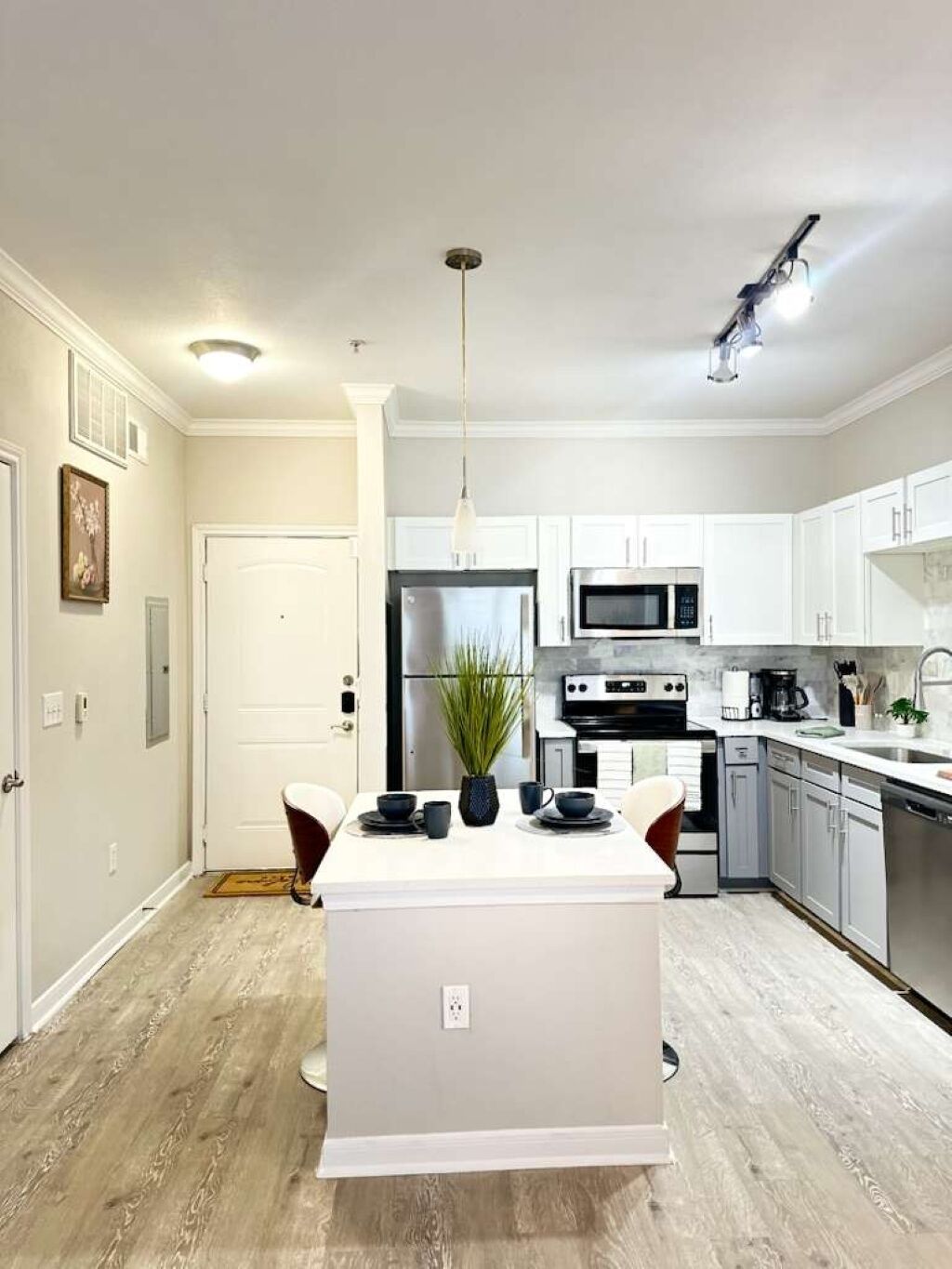 Una cocina moderna con gabinetes blancos, una isla central, electrodomésticos de acero inoxidable y una lámpara colgante.