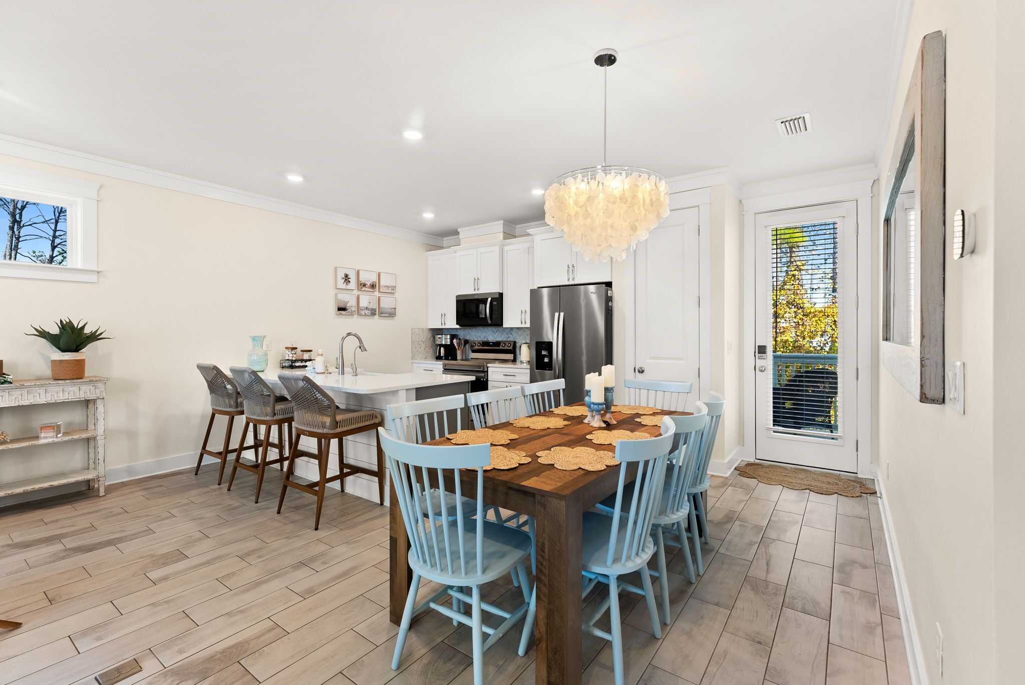 Une cuisine moderne avec des meubles blancs, un îlot central et un coin repas agrémenté de chaises bleues et d’une table en bois.