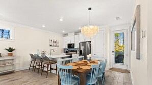 Une cuisine moderne avec des meubles blancs, un îlot central et un coin repas agrémenté de chaises bleues et d’une table en bois.