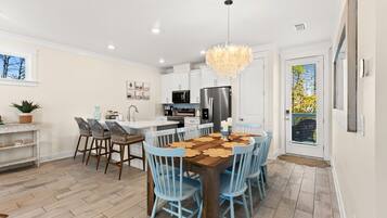 Une cuisine moderne avec des meubles blancs, un îlot central et un coin repas agrémenté de chaises bleues et d’une table en bois.