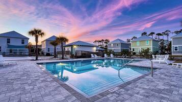 Ein Pool mit Liegestühlen und einem Zaun, umgeben von Häusern unter einem Sonnenuntergangshimmel.