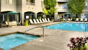 A swimming pool with lounge chairs and umbrellas, surrounded by a building with balconies and trees. - 3-Bedroom Condo in the Heart of the City (Salt Lake City)