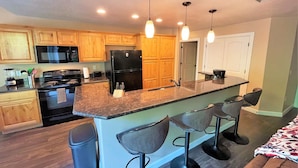 A modern kitchen with wooden cabinets, a black refrigerator, a stove, and a bar area with stools. - 3-Bedroom Condo in the Heart of the City (Salt Lake City)