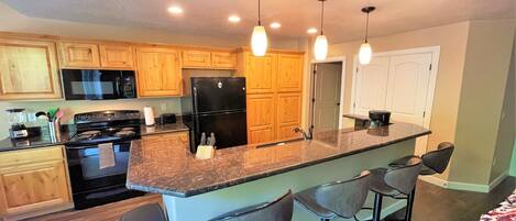 A modern kitchen with wooden cabinets, a black refrigerator, a stove, and a bar area with stools.