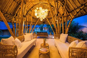 Estrutura interior de bambu com mobiliário de vime e um lustre central.