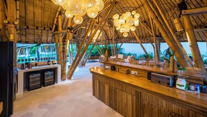 Un espace bar décoré sur le thème du bambou, avec un comptoir, des sièges et des luminaires suspendus.