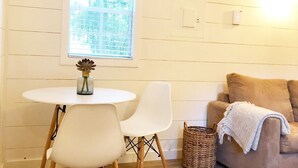A cozy room with a round table, two chairs, a wicker basket, and a beige sofa with a throw blanket. - Lost River Tiny House, dog-friendly + hot tub (Mathias)