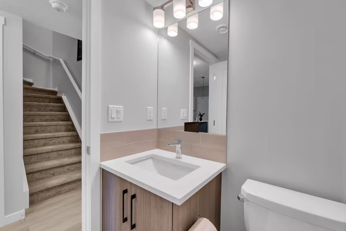 Een moderne badkamer met een wit wastafel, spiegel en toilet.