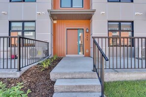 A modern building with a wooden front door, a small porch, and a metal railing. - Modern 2BR Townhome in Belmont with AC & Parking (Calgary)