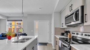 A modern kitchen with a central island, stainless steel appliances, and a view to the outside. - Modern 2BR Townhome in Belmont with AC & Parking (Calgary)