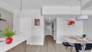 A modern kitchen with white cabinetry, a central island with a red plant, and a dining area with a white table and chairs. - Modern 2BR Townhome in Belmont with AC & Parking (Calgary)