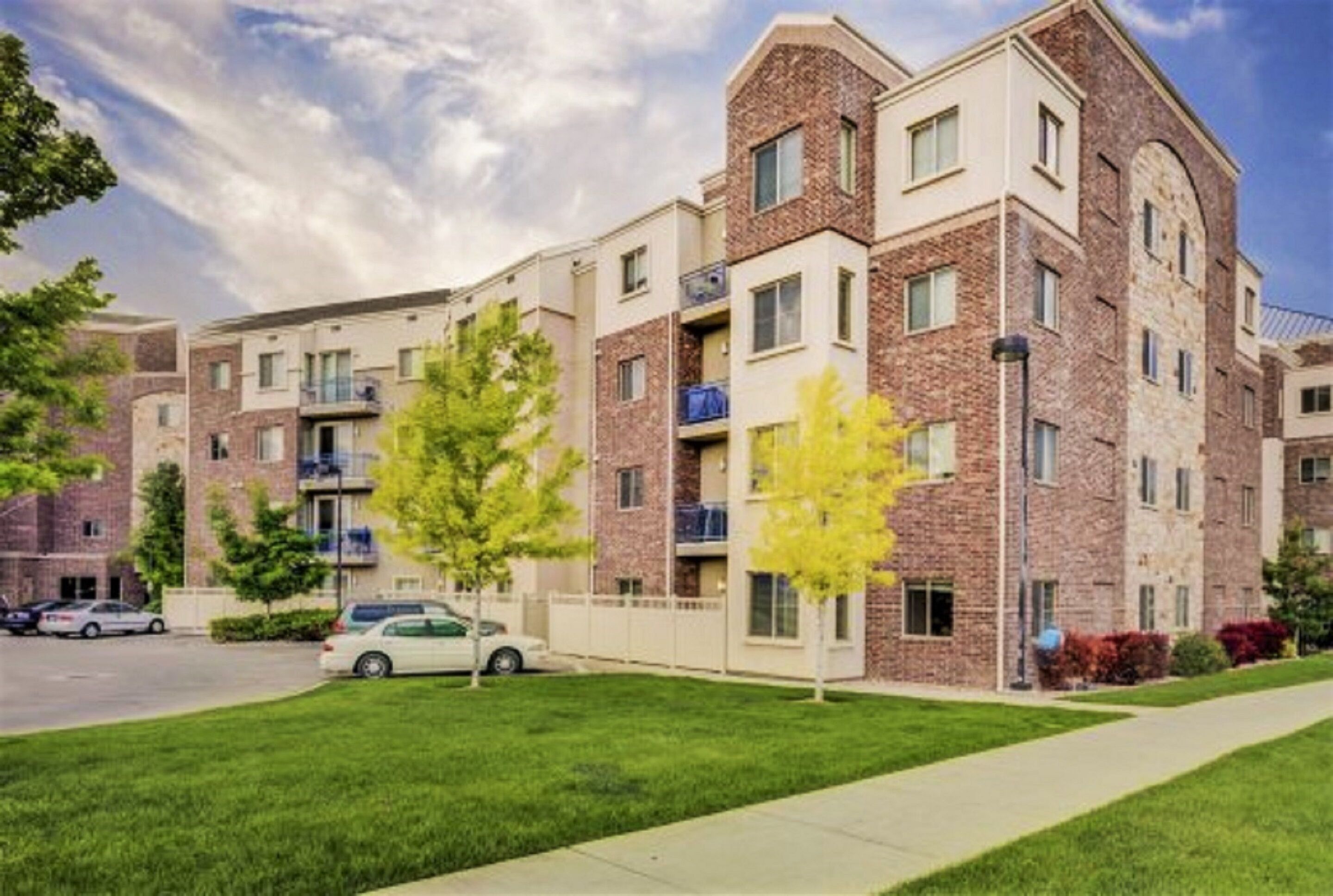 A multi-story residential building with brick exterior, balconies, and a well-maintained lawn.