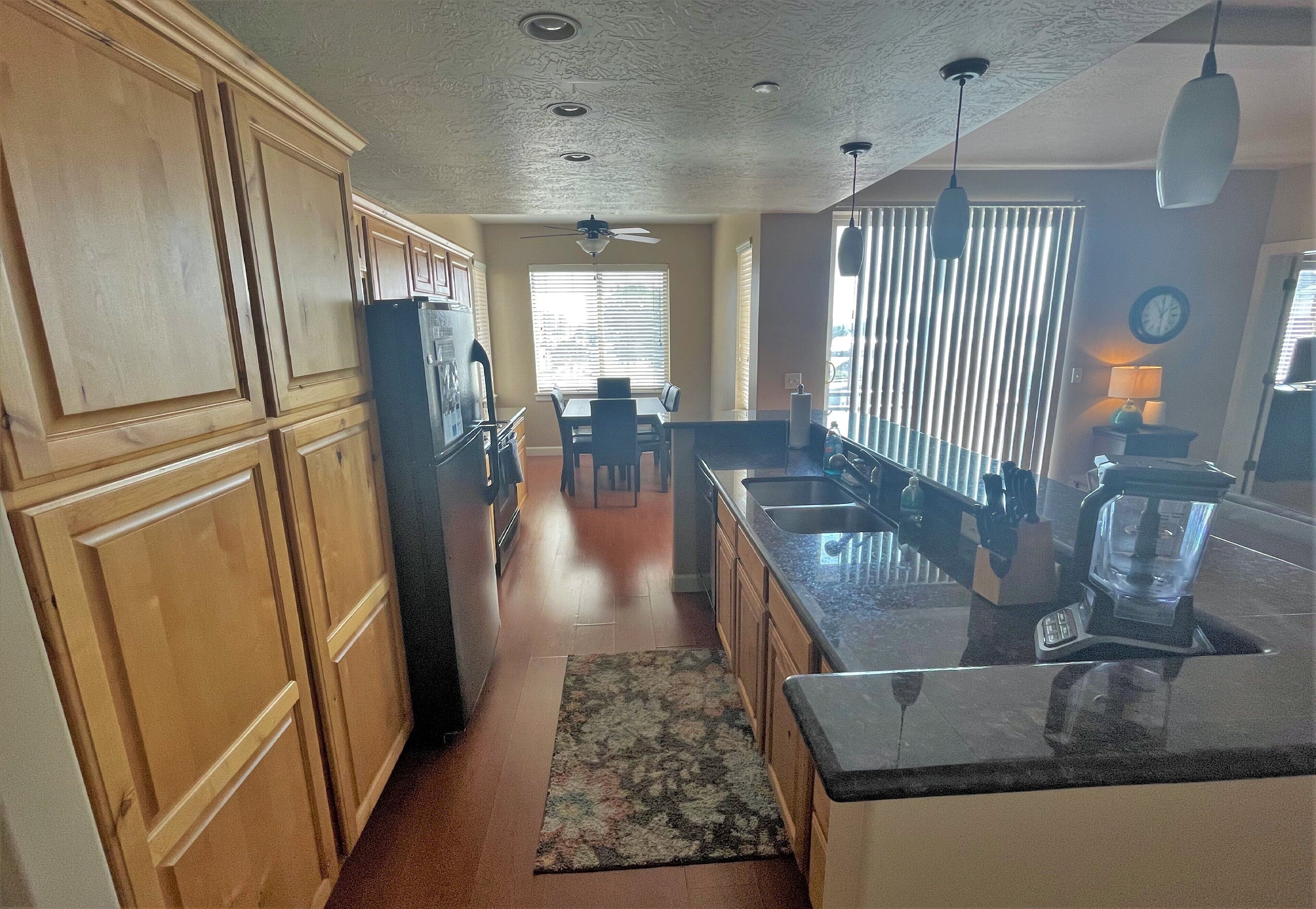 Una cocina con armarios de madera, encimera de granito, refrigerador y un comedor con mesa y sillas.