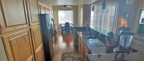 Una cocina con armarios de madera, encimera de granito, refrigerador y un comedor con mesa y sillas.
