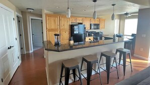 A kitchen with wooden cabinets, a black refrigerator, a microwave, and a bar area with stools. - Downtown Condo Close to Everything (Salt Lake City)