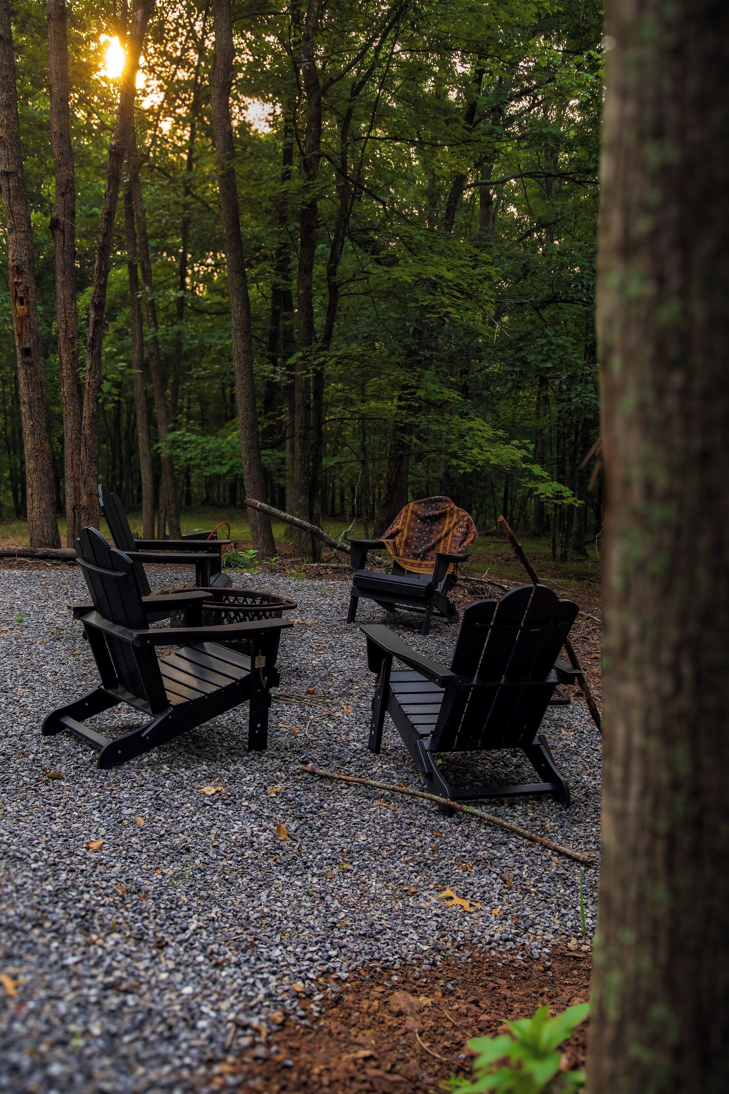 Un terrain de camping situé dans une forêt, équipé de chaises Adirondack et d’un foyer.