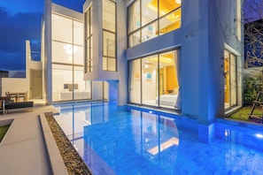 A modern house with a swimming pool, large windows, and a well-lit interior. - Luxpride4 (Si Sunthon)