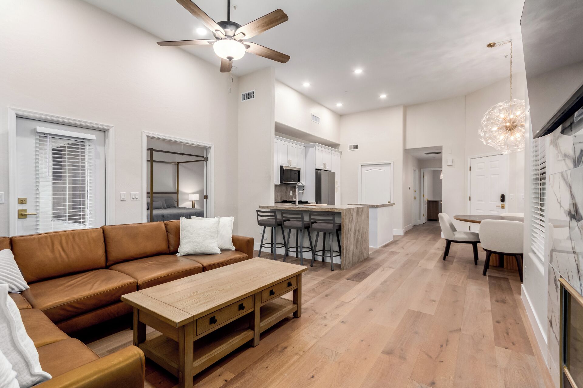 A modern living room with a brown leather sofa, a wooden coffee table, and a ceiling fan.