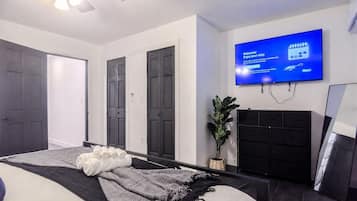 A modern hotel room with a bed, a flat-screen TV, a plant, and a black dresser.