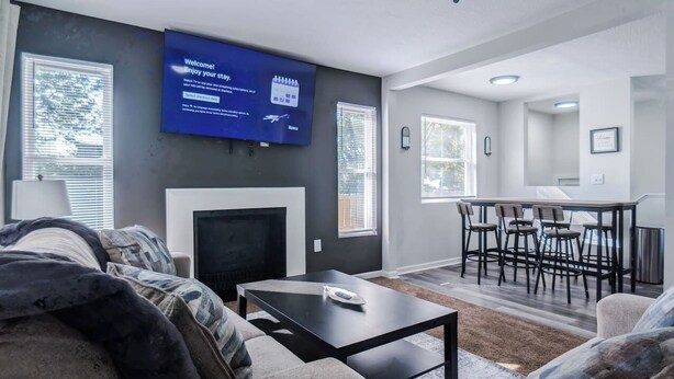 Een moderne woonkamer met een flatscreen televisie, een open haard, een eethoek met barkrukken, en een keuken op de achtergrond.