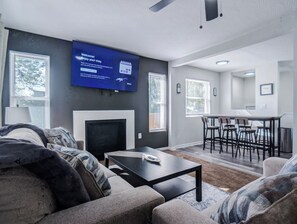 Ein modernes Wohnzimmer mit Flachbildfernseher, Kamin, Essbereich mit Barhocker und einer Küche im Hintergrund.