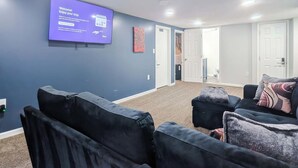 Hotelkamer met een groot scherm waarop een welkomstboodschap staat, een donkerblauwe wand, een tapijtvloer en een zithoek met een bank en poef.