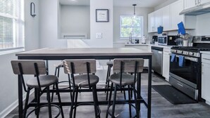 Een moderne keuken met een centraal eiland, barstoelen, roestvrijstalen apparatuur en witte kastjes.