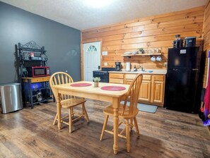 Eine kleine Küche mit Holzausstattung, einem Esstisch mit Stühlen, einem Kühlschrank und einer Mikrowelle.