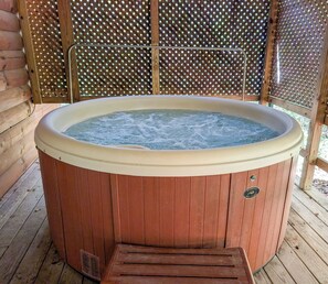 A wooden hot tub with a metal ladder, surrounded by a wooden deck and a lattice fence. - Couples Cabin with Hot Tub, Grill, Firepit & EV (Logan)