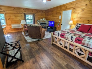Ein Blockhauszimmer mit einem Bett, einem Sessel, einem Kamin, einem Fernseher und einem Holzboden.
