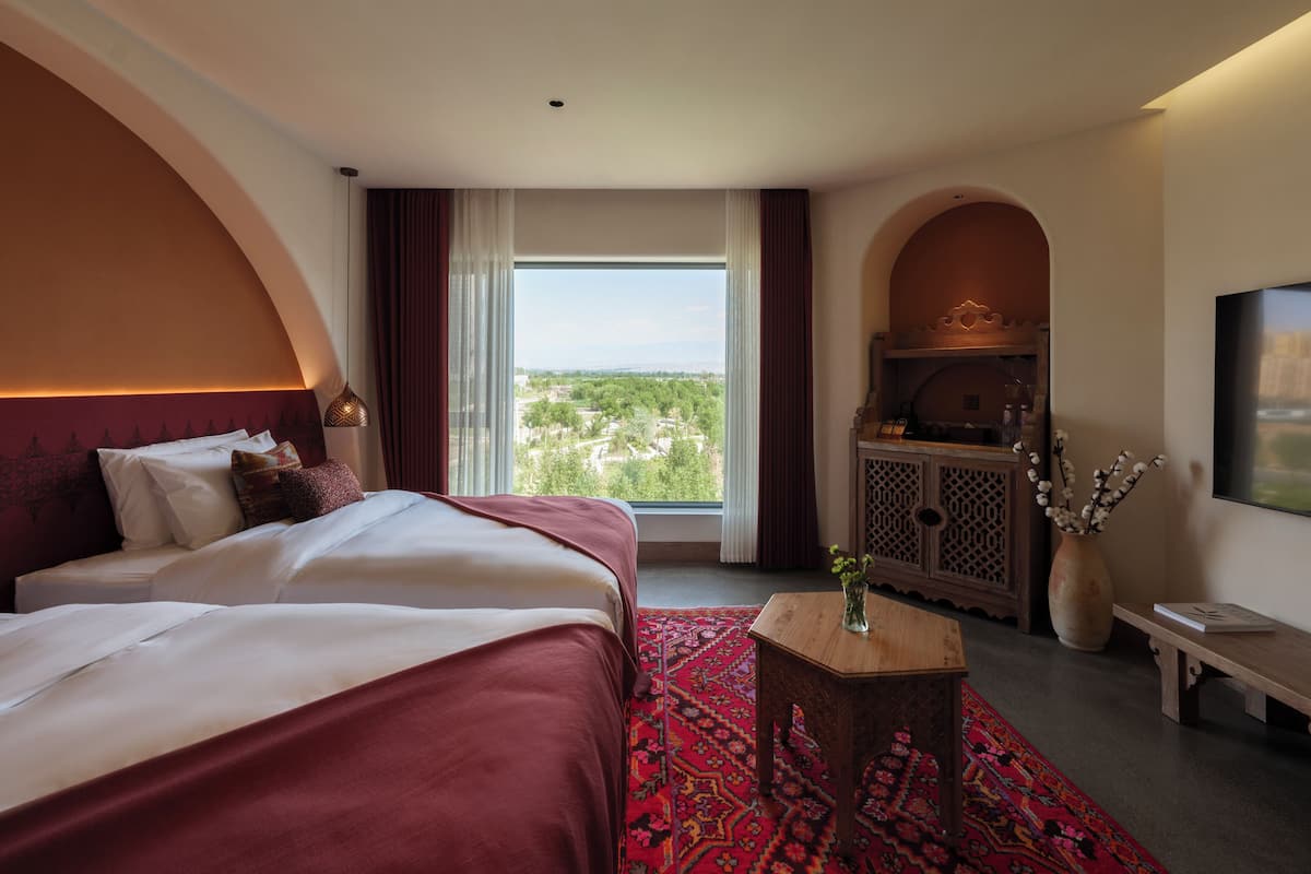 A hotel room with a large bed, a small table, a TV, and a view of the city.