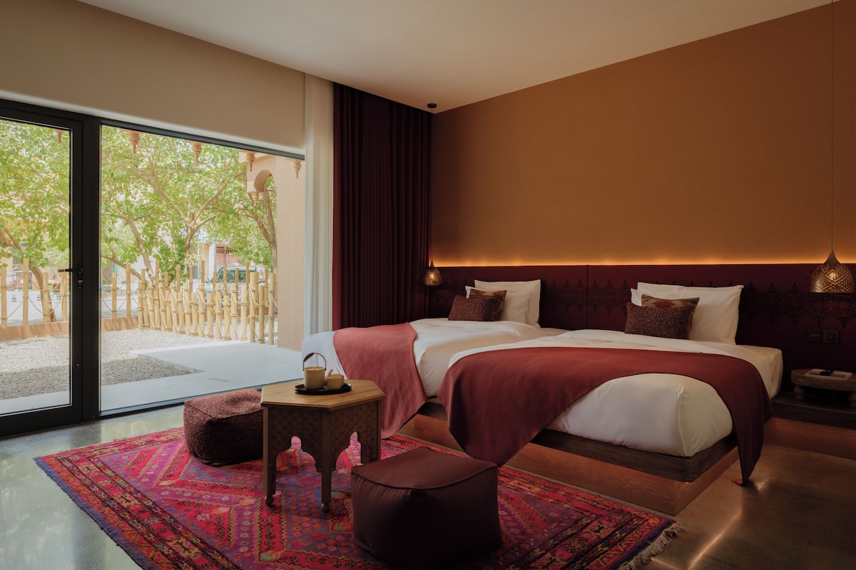 Una habitación de hotel moderna con una cama grande, una mesita auxiliar pequeña, un tapete decorativo y vistas al exterior.