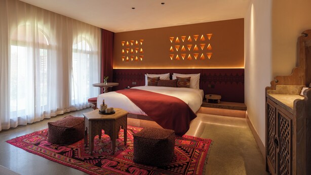 A hotel room with a large bed, a small round table, a decorative rug, and a wooden cabinet.
