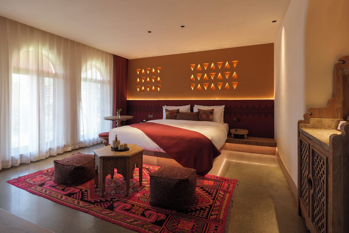 A hotel room with a large bed, a small round table, a decorative rug, and a wooden cabinet.