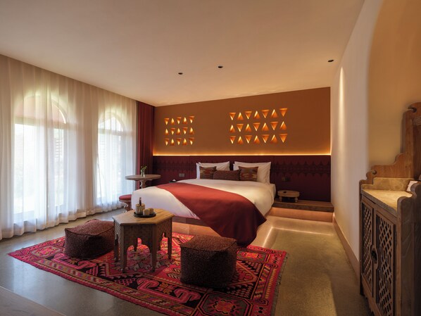 A hotel room with a large bed, a small round table, a decorative rug, and a wooden cabinet.