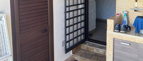 A room with a tiled floor, a wooden door, a metal gate, a tiled wall, a small sink, and a towel hanging on the wall.