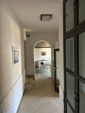 A hallway with a tiled floor, a white-framed picture on the left, a door with a handle on the right, and a kitchen area in the background.