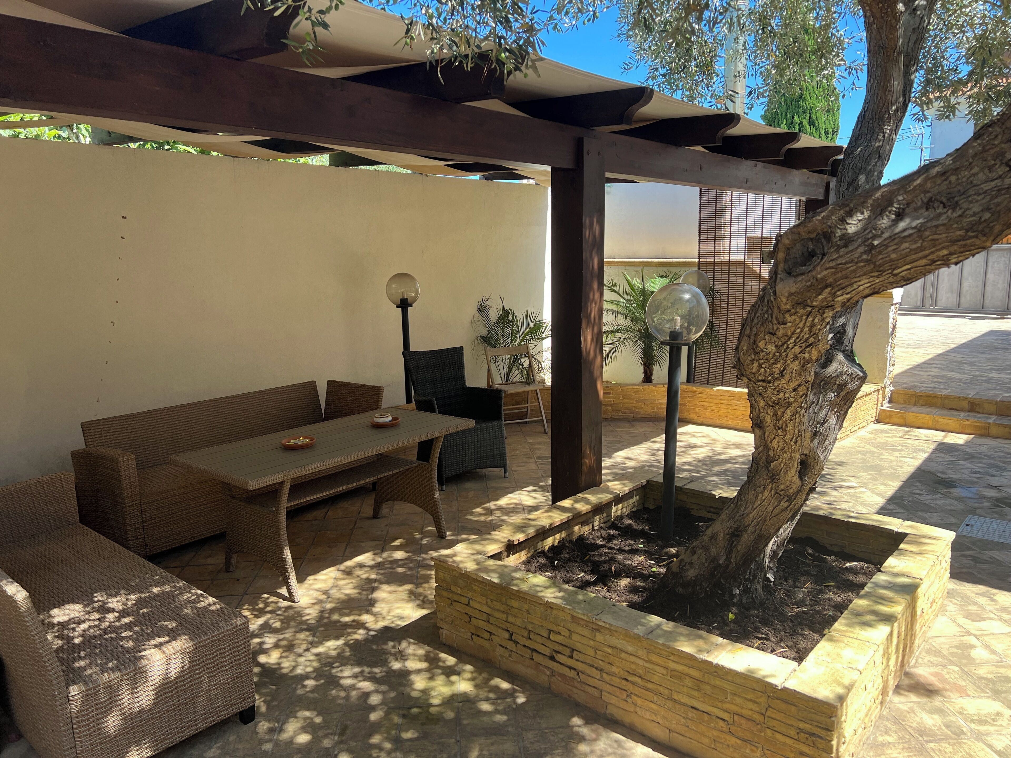 An outdoor patio area with wicker furniture, a table, and a planter with a tree.