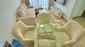 Un salón con un sofá color beige, una mesa de centro de vidrio y un televisor montado en la pared.