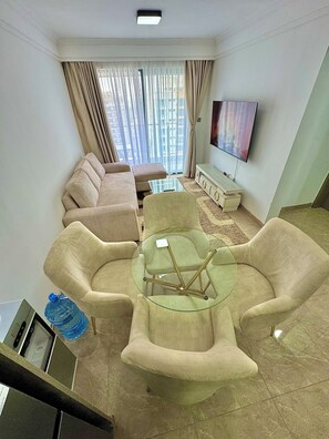 Ein Wohnzimmer mit einem beigen Sofa, einem Glastisch und einem an der Wand montierten Fernseher.