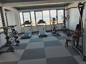Ein Fitnessstudio mit Laufbändern, Krafttrainingsgeräten und Blick auf die Stadt durch große Fenster.